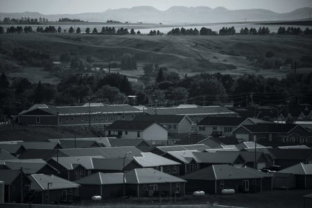 Black and white photograph showing homes in a neighborhood and landscape in the background.