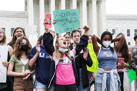 Women holding signs gather in front of the Supreme Court.