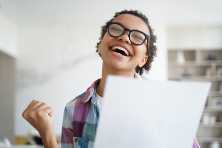 Happy female student makes "yes" gesture, holding document, celebrating success