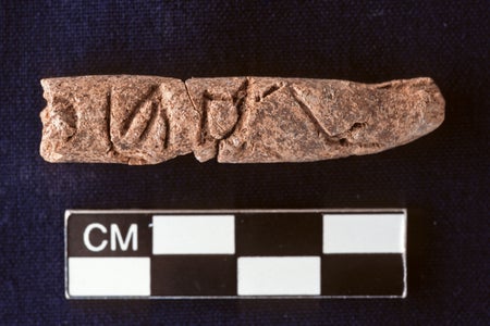 Photograph of clay artifact, roughly the size of a finger, on a black surface