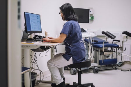 Side view of a doctor using desktop PC sitting at desk inside a clinic's patient exam room