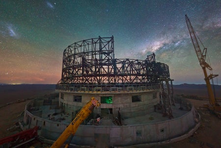 A webcam image of the construction site of ESO’s Extremely Large Telescope at Cerro Armazones, in Chile's Atacama Desert. Behind the steel structure of the partially built telescope, the starry sky is dominated by the core of the Milky Way and the Large and Small Magellanic clouds