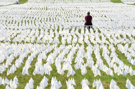 A woman shown from behind amid thousands of white flags at a COVID memorial at the National Mall.