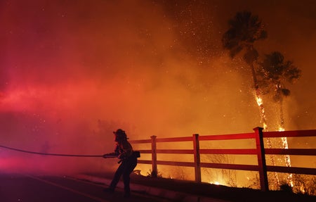 A firefighter pulls a water hose through fire