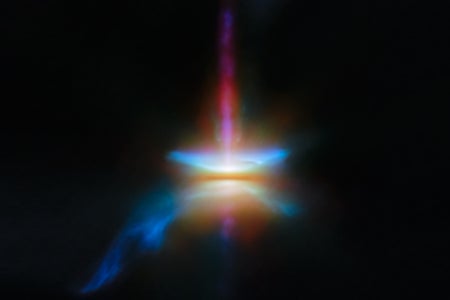 A close-in image of a protoplanetary disc around a newly formed star. Many different wavelengths of light are combined and represented by separate and various colours. A dark line across the centre is the disc, corresponding to the densest parts of the disc, made of opaque dust: the star is hidden in here and creates a strong glow in the centre. A band going straight up is a jet, while other outflows above and below the disc, and a tail coming off to one side