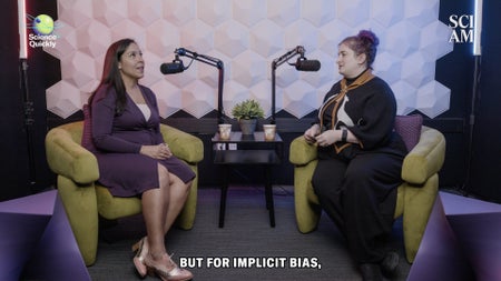 Two women sit on green chair speaking into microphones