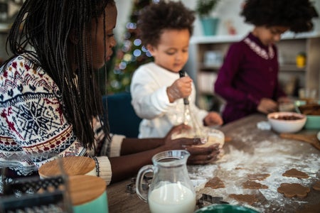 Parent baking cookies with their two children at a kitchen table during the holidays