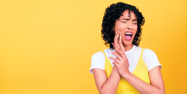 A woman holding her cheek in pain, against a yellow background