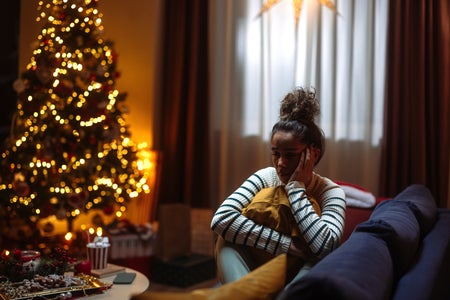 A woman looks melancholy; a festive Christmas tree appears in the background