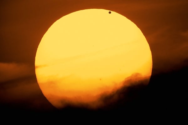 Photograph of Venus transiting the sun which is partially obscured by clouds in the sky