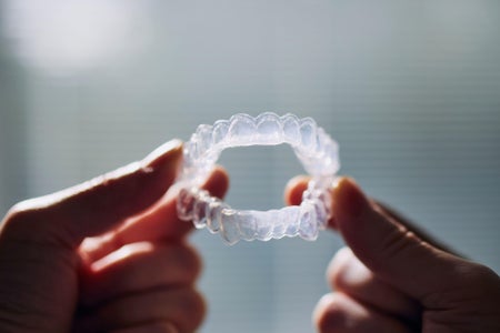 Close-up view of hand holding teeth whitening trays against window.